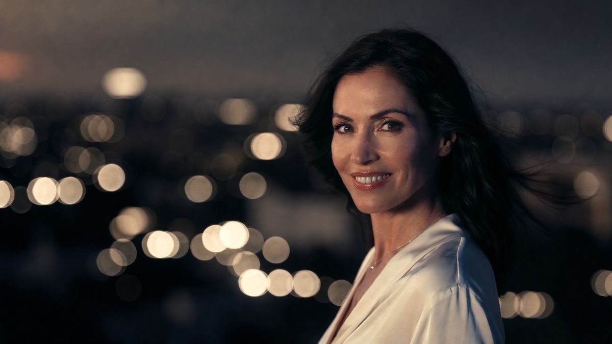 A smiling woman in a white silk blouse against city lights at dusk
