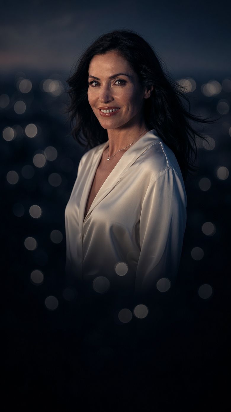 A smiling woman in a white silk blouse against city lights at dusk